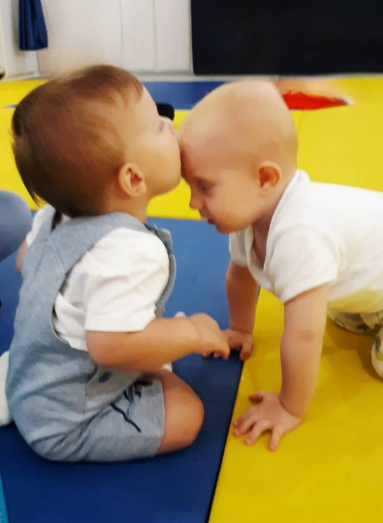 Baby kissing another baby's forehead